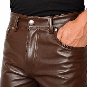 May include: Dark brown leather trousers featuring a high-waisted design with belt loops, a central silver-toned button closure, and two front pockets. The smooth, polished material has a subtle sheen, and the construction includes visible stitching.