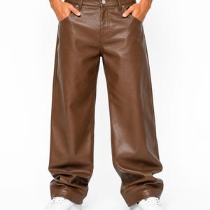 Könnte beinhalten: Braune Hose aus Kunstleder mit weitem Bein, ausgestattet mit einem klassischen Fünf-Taschen-Design, einem Knopf- und Reißverschluss sowie Gürtelschlaufen am Bund. Die Hose hat eine glatte, halbmatte Oberfläche und eine lockere Passform.