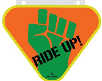 Może przedstawiać: Żółty znak w kształcie trójkąta z pomarańczowym tłem i uniesioną w górę zieloną pięścią. Tekst "RIDE UP!" jest napisany czarnym kolorem na pięści. Na dole znaku znajduje się tekst "CYCLETAGS.COM" w kolorze czarnym.