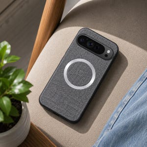 May include: A rectangular smartphone case featuring a textured dark gray fabric finish on the back. The case includes a prominent silver circular magnetic ring centered on the rear surface and a black camera module cutout at the top.