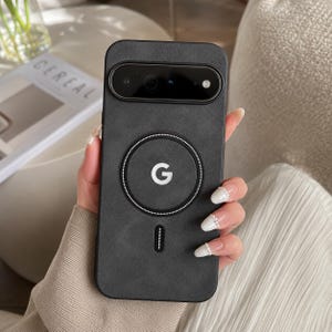 Op de afbeelding: Een zwarte smartphonehoes met een matte textuur, voorzien van een opvallende cirkelvormige magnetische oplaadring in het midden met een wit G-logo. De hoes heeft een horizontale uitsparing voor de camera aan de bovenkant en een kleine verticale gleuf.