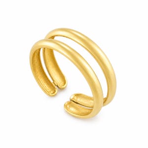 Puede incluir: Un anillo de tono dorado con un diseño de doble banda y un acabado liso y redondeado. El anillo tiene una estructura abierta que permite su ajuste y muestra un color amarillo metálico consistente en toda su superficie.