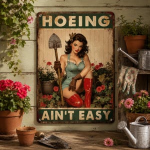 May include: A rectangular metal sign featuring a pin-up style illustration of a person in a green outfit and red boots holding a shovel, with the text HOEING AIN'T EASY printed in bold letters at the top and bottom against a light wood background.
