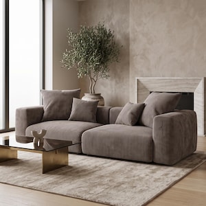Pode incluir: Um sofá modular seccional estofado em tecido de veludo cotelê na cor taupe, com braços largos e quatro almofadas quadradas correspondentes. O sofá apresenta um design de perfil baixo com assentos profundos e uma superfície canelada.