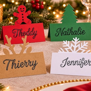 Könnte beinhalten: Vier gefaltete Tischkarten aus Karton mit weihnachtlichen Aufsätzen. Eine rote Karte mit Lebkuchenmann zeigt Theddy, eine grüne mit Tannenbaum zeigt Nathalie, eine beige mit Rentiergeweih zeigt Thierry und eine weiße mit Schneeflocke zeigt Jennifer.