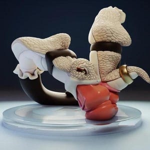 Op de afbeelding: Een sculpturaal beeldje met een textuurrijke, gebroken witte, reptielachtige vorm met een gebogen lichaam, voorzien van een zwarte band en een gouden ring. Het figuur heeft een gladde, koraalkleurige basis en rust op een rond, doorschijnend platform.
