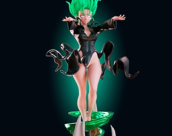 Può includere: Una statuetta di un personaggio con capelli verde brillante e occhi bianchi, che indossa un body nero a maniche lunghe con un design a gamba alta. La figura poggia su una base rocciosa marrone circondata da un effetto di energia verde vorticosa.