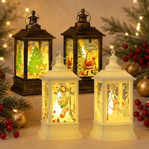 May include: Four decorative holiday lanterns featuring festive scenes. Two lanterns have a dark bronze finish with illustrations of a Christmas tree and Santa Claus. Two lanterns are white with images of a Christmas stocking and a snowman.