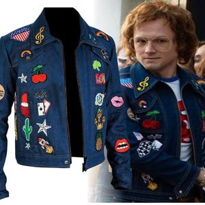 May include: A dark blue denim jacket featuring a variety of colourful embroidered patches including cherries, a rocket, a cactus, lips, a pineapple, a mushroom, playing cards, a treble clef, a rainbow, and an American flag on the chest and sleeves.