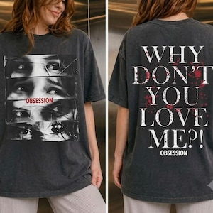 May include: A charcoal gray short-sleeve t-shirt featuring a graphic of fragmented eyes and the word OBSESSION on the front. The back displays the text WHY DON'T YOU LOVE ME?! in white with red blood-like splatters and the word OBSESSION below.