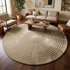 May include: A large, circular area rug in a solid beige tone, featuring a carved, recessed pattern of concentric circles in the centre and curved, segmented lines radiating outward toward the edges, creating a textured, geometric design.