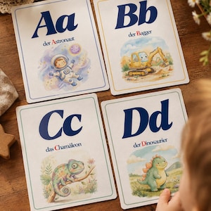 Op de afbeelding: Vier rechthoekige educatieve kaarten met de letters Aa, Bb, Cc en Dd. Elke kaart toont een donkerblauwe letter, een Duits woord en een aquarelillustratie: een astronaut, een gele graafmachine, een kameleon en een dinosaurus.