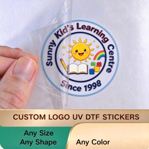 May include: A circular sticker featuring a smiling yellow sun, an open book, a pencil, a rainbow, and colourful building blocks. The text reads Sunny Kid's Learning Centre Since 1998. The sticker is being peeled from a clear backing sheet.