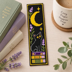 Puede incluir: Un marcapáginas rectangular de punto de cruz que muestra un gato negro sentado sobre una pila de tres libros bajo una luna creciente amarilla y estrellas, decorado con ramas de lavanda moradas y enmarcado por un fino borde amarillo.