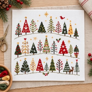 Könnte beinhalten: Ein weißes Stoffquadrat mit einem Kreuzstichmuster aus verschiedenen Weihnachtsbäumen, die in drei horizontalen Reihen angeordnet sind. Die Bäume sind in Rot-, Grün- und Goldtönen gehalten und mit kleinen Sternen, einem Vogel und einer Hirschsilhouette verziert.