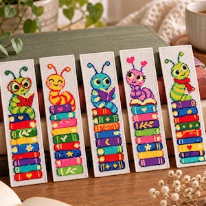 Peut inclure: Cinq marque-pages rectangulaires en point de croix représentant des chenilles de dessin animé colorées perchées sur des piles de livres. Chaque chenille a une expression et une couleur uniques, incluant le vert, le jaune, le bleu et le rose.