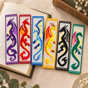 May include: Six rectangular plastic canvas bookmarks featuring pixelated dragon designs in purple, red, blue, yellow, black, and green. Each bookmark has a matching coloured border with a checkered pattern at the top and bottom edges.