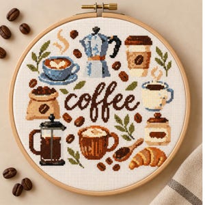 Op de afbeelding: Een ronde houten borduurring met een kruissteekpatroon op witte stof. Het ontwerp toont het woord coffee in bruin handschrift, omringd door diverse koffie-gerelateerde iconen zoals een moka-pot, cafetière, mokken, koffiebonen en een croissant.
