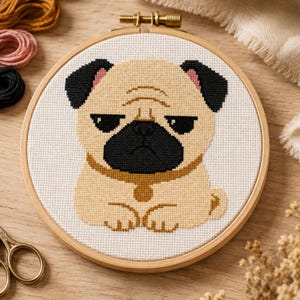 May include: A cross-stitch embroidery project featuring a tan pug with a black muzzle, black ears, and a tan collar, centered within a round wooden embroidery hoop. The design is stitched onto white fabric, showcasing detailed pixelated dog features.