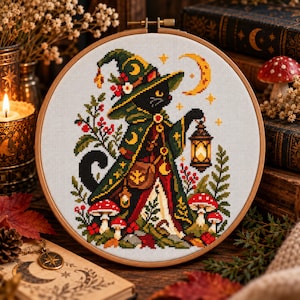 Peut inclure: Un tambour à broder circulaire en bois contenant un motif au point de croix représentant un chat noir vêtu d'une cape et d'un chapeau pointu verts, tenant une lanterne allumée. Le motif inclut des champignons rouges et un croissant de lune.