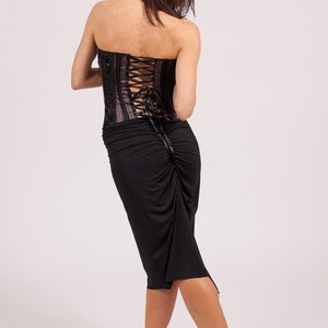May include: A woman wearing a black skirt and a pink and black corset with a lace-up back.