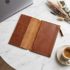 May include: A tan leather travel wallet featuring an open interior with multiple card slots on the left side and a zippered compartment on the right side. The wallet is constructed from smooth, durable leather with visible stitching and a metal zipper pull.