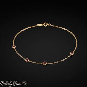 Può includere: Un delicato bracciale a catena in oro con quattro pietre preziose rosse rotonde, incastonate a lunetta e distanziate uniformemente. Il bracciale include un piccolo meccanismo di chiusura in oro nella parte superiore per questo gioiello.