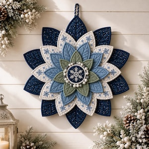 May include: A layered fabric wall hanging shaped like a star or flower with pointed petals in navy blue, light blue, sage green, and white. The design features quilted textures, snowflake patterns, and a central circular medallion with a white snowflake.
