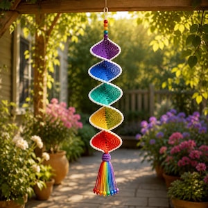 May include: A vertical hanging decoration featuring a spiral of crocheted diamond-shaped segments in a rainbow gradient of purple, blue, teal, green, yellow, orange, and red, topped with small colorful beads and finished with a rainbow tassel.