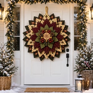 Peut inclure: Une couronne en tissu matelassé composée de pétales superposés en forme d'étoile aux motifs bordeaux, vert olive et crème à carreaux. Le centre présente une plaque en bois circulaire avec un flocon de neige, entourée de baies rouges et de pommes de pin.