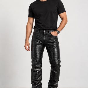 May include: Black trousers featuring a textured crocodile skin pattern, a button and zip fly closure, and belt loops. The trousers are paired with a plain black short-sleeved t-shirt. The Legend Leather logo is visible in the top left corner.