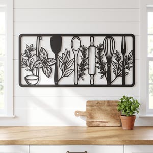 May include: A rectangular black metal wall art piece featuring a cutout design of various kitchen utensils including a ladle, spatula, spoon, rolling pin, whisk, and fork, interspersed with detailed illustrations of fresh green herbs.