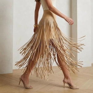 May include: A beige sleeveless tank top paired with a high-waisted tan skirt featuring a wide waistband and long, flowing fringe detailing that extends from the mid-thigh down to the lower calf, creating a dynamic movement effect.