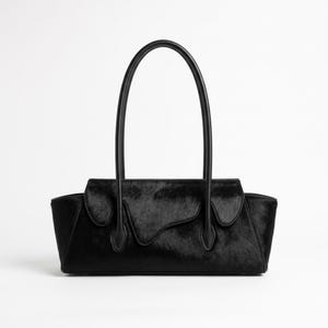 May include: A black handbag with a textured hair-on-hide finish, featuring a horizontal rectangular body, a curved flap closure with an irregular edge, and two tall, slender, smooth leather shoulder straps attached to the front panel.