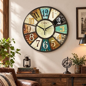 Può includere: Un grande orologio da parete rotondo con una cornice in metallo scuro e un quadrante segmentato multicolore. Ogni segmento presenta una diversa consistenza e colore usurato, mostrando grandi numeri da 1 a 12. Il centro è color crema con il testo SICILIAN OLIVE.