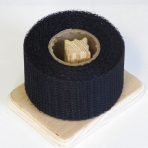 May include: A roll of black hook and loop tape on a wooden spool. The tape is used for attaching items together.