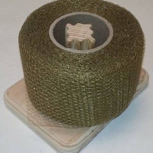 May include: A roll of olive green metallic mesh ribbon on a wooden spool. The ribbon is wrapped around the spool and is ready to be used for crafting or decorating.