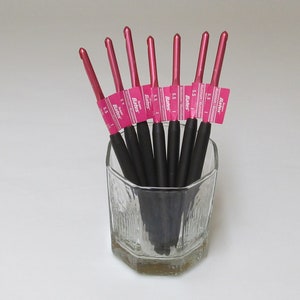 May include: A set of seven pink crochet hooks with black handles, labeled with the size "5.5" and the brand "Boye" in a clear glass cup.