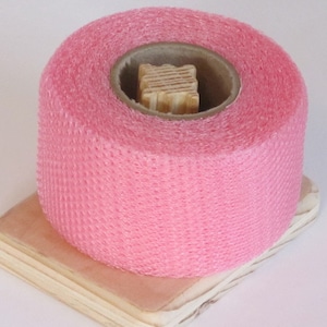 May include: A roll of pink, mesh-like tape on a wooden spool. The tape is textured and has a honeycomb pattern.