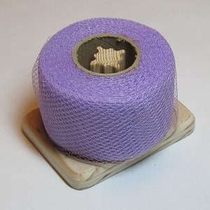 May include: A spool of lavender tulle fabric on a wooden base. The tulle is a fine, sheer mesh fabric with a delicate texture.