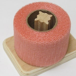 May include: A roll of peach-coloured netting on a wooden spool. The netting is a fine mesh and is wrapped around the spool.