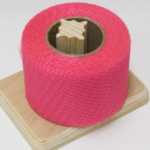 May include: A roll of pink netting on a wooden spool with a wooden base.