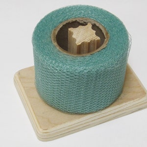 May include: A roll of teal green netting on a wooden spool, sitting on a square wooden base.