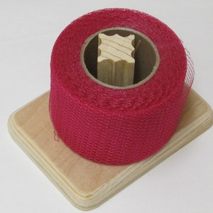 May include: A roll of pink netting on a wooden spool, sitting on a wooden base.