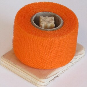 May include: A roll of bright orange netting on a wooden spool. The netting is made of a fine mesh material.