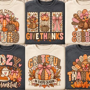 May include: A collection of six crewneck sweatshirts in cream and charcoal gray, each featuring colorful Thanksgiving-themed graphic prints including pumpkins, turkeys, and autumn leaves with text such as Oh My Gourd, Give Thanks, Gobble Gobble, Cozy & Thankful, Grateful In Every Season, and Thankful.