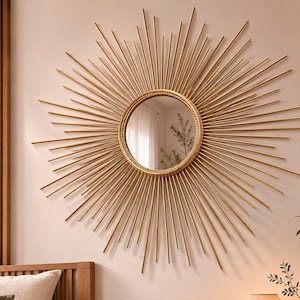 Könnte beinhalten: Ein runder Wandspiegel mit einem goldenen Strahlenkranz-Rahmen aus zahlreichen dünnen, radial angeordneten Metallstäben. Das zentrale Glas ist kreisförmig und von einem strukturierten, seilartigen Rand umgeben, der einen sternförmigen Effekt erzeugt.
