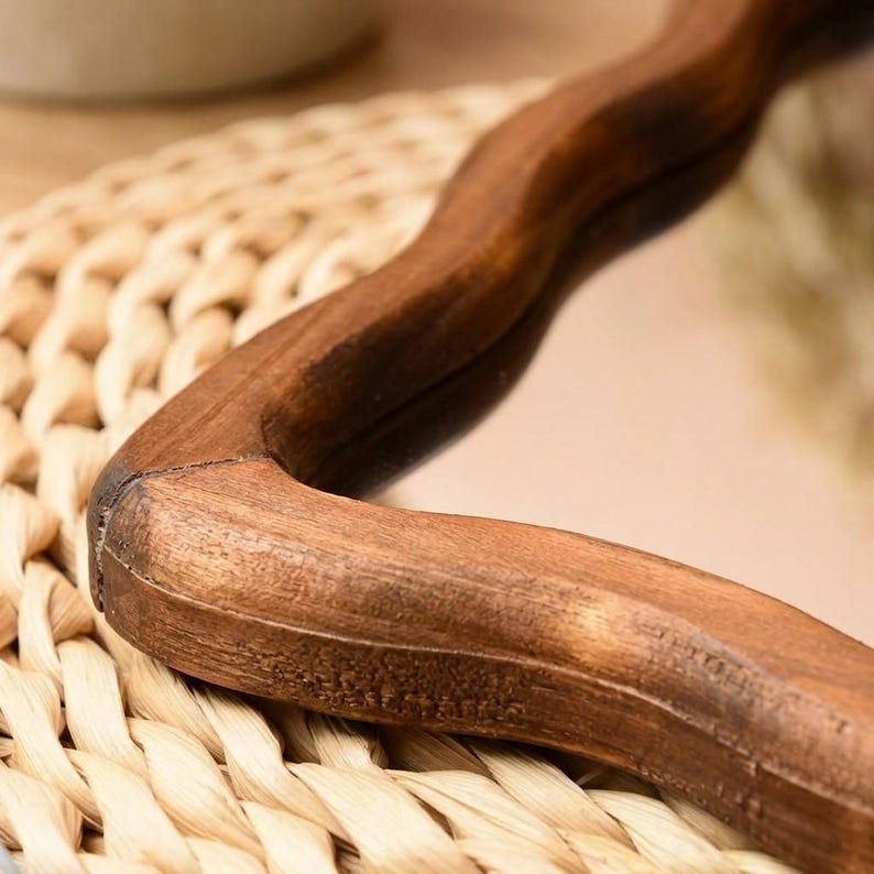 Close-up detail of wavy mirror frame in warm natural wood, showing organic curves, wood grain and handcrafted sculptural design.
