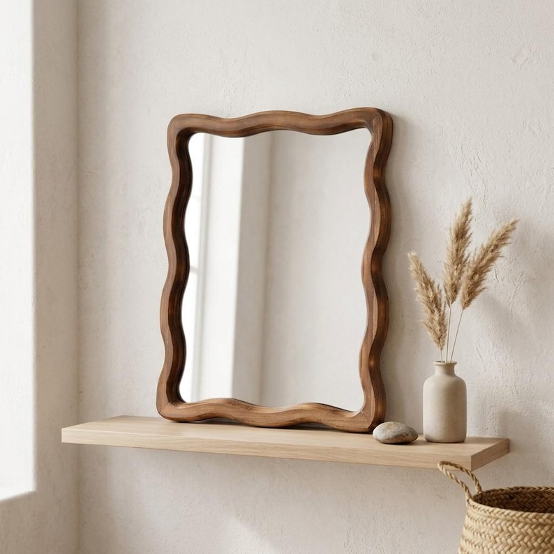 Wavy wood framed mirror displayed on a floating shelf, organic irregular wall mirror for minimalist Japandi and wabi sabi decor.