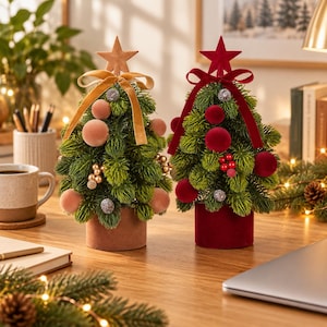 May include: Two artificial tabletop Christmas trees with green needles. The left tree features a tan star, tan velvet ribbon, and tan ornaments. The right tree features a red star, red velvet ribbon, and red ornaments. Both sit in cylindrical bases.